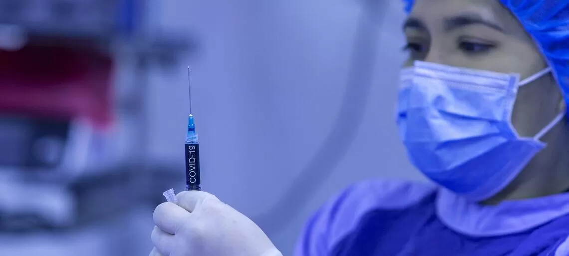 infermiera con camice e mascherina maneggia siringa con vaccino