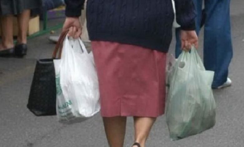 Donna anziana di spalle che trasporta buste della spesa