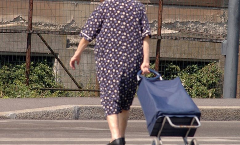 Donna anziana di spalle che porta un carrello