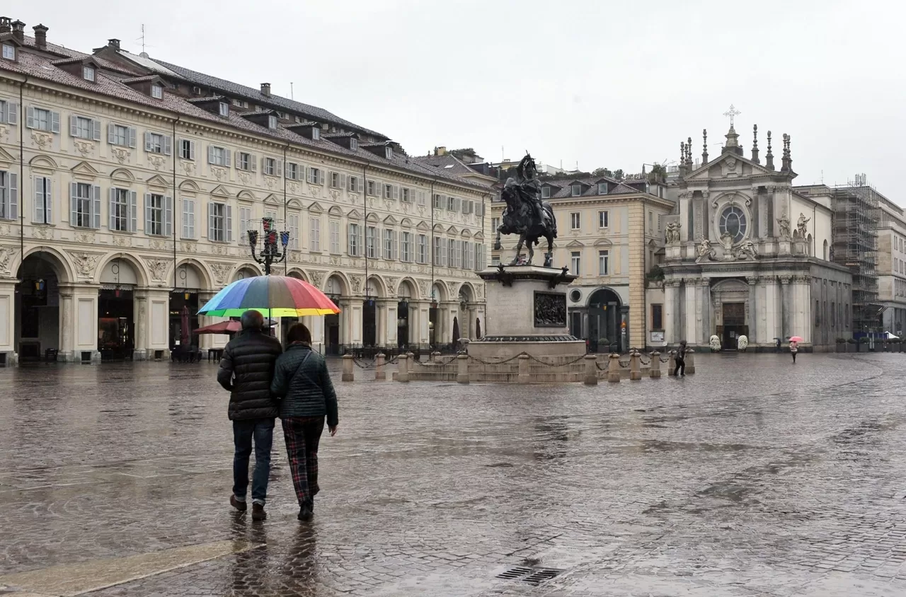 uomo e donna camminano a braccetto in piazza San Carlo coperti da un ombrello arcobaleno sotto la pioggia