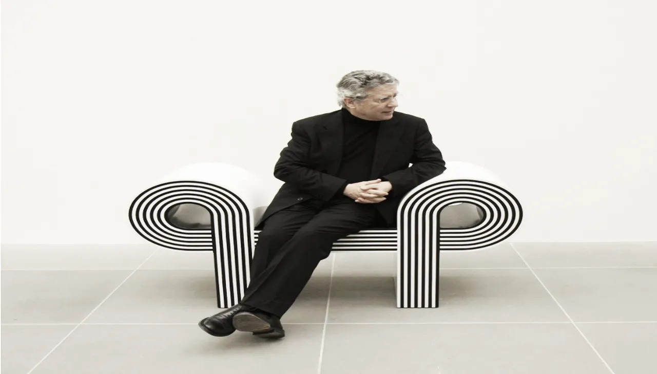 Marcello Morandini seduto su una sedia di design in bianco e nero con linee geometriche curve, indossa un completo nero e guarda di lato in un ambiente minimalista