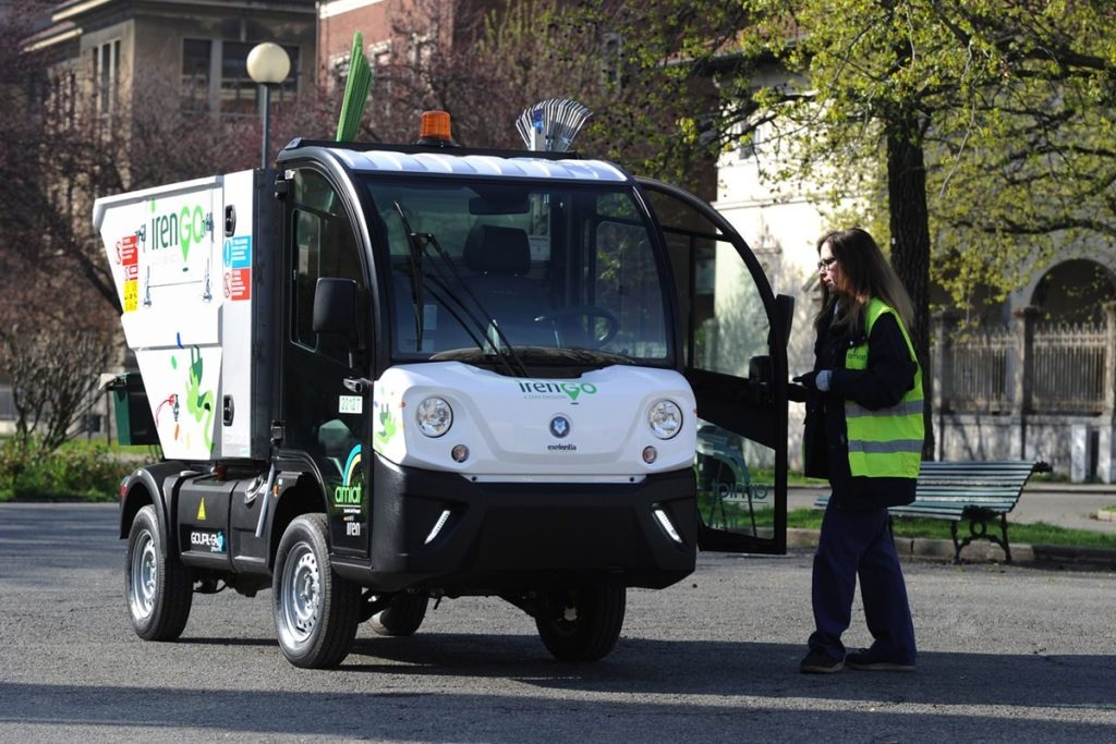 Veicolo elettrico Amiat Torino del Gruppo Iren per la raccolta rifiuti, con operatrice ecologica in divisa al lavoro in un parco urbano