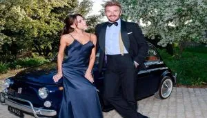 David Beckham, elegantissimo in smoking, posa sorridente accanto a sua moglie Victoria davanti a una Fiat 500 d’epoca nera: un omaggio al design italiano per celebrare i suoi 50 anni