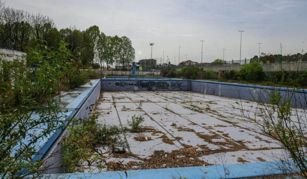 Piscina scoperta delle Sempione a Torino in stato di abbandono, con vasca vuota, erbacce e segni di degrado in attesa di riqualificazione
