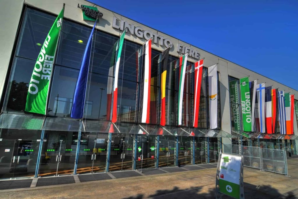 Ingresso principale del Lingotto Fiere di Torino, sede del Salone del Libro di Torino 2025, con bandiere internazionali esposte sulla facciata.