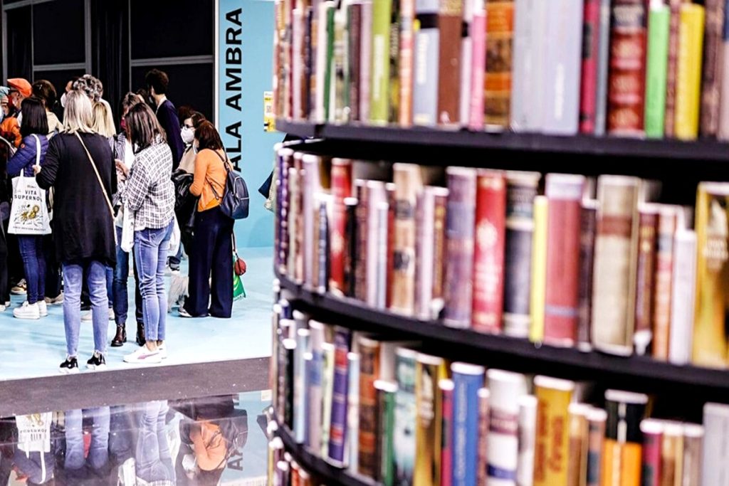 Visitatori in attesa di un evento nella Sala Ambra del Salone del Libro di Torino 2025, con una libreria in primo piano colma di volumi