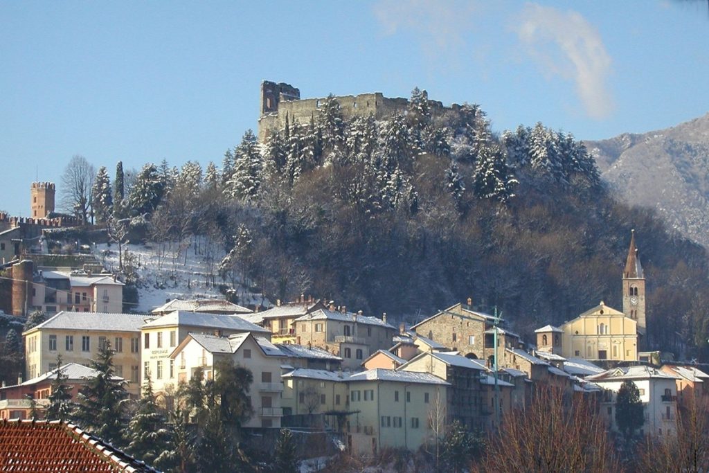 Il Castello di Avigliana visto in inverno, innevato sopra il borgo storico, con tetti e colline ricoperti di neve nella Valle di Susa