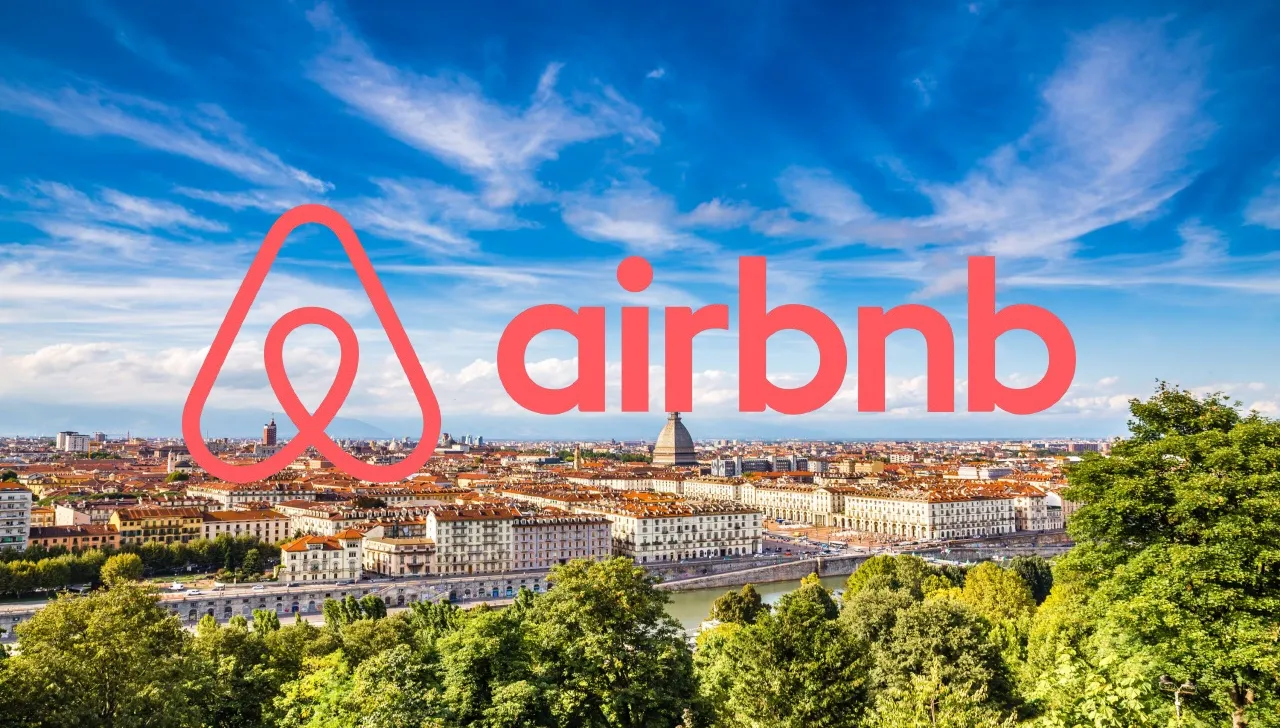 Logo Airbnb sovrapposto a una panoramica del centro di Torino con la Mole Antonelliana sullo sfondo, visto da Monte dei Cappuccini
