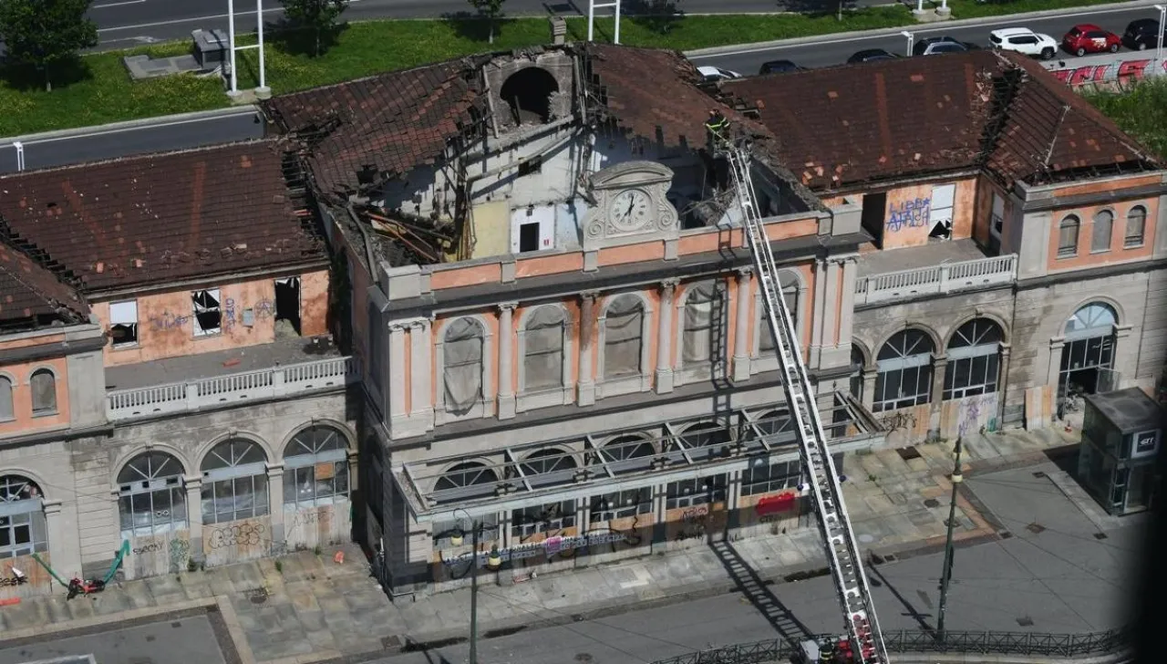 Facciata danneggiata della vecchia stazione di Porta Susa a Torino dopo il crollo del tetto, con vigili del fuoco sul posto e scritte sui muri