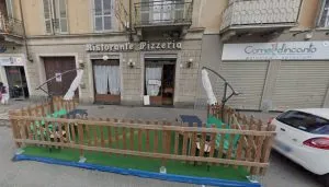 Esterno del ristorante-pizzeria Spiga d’Oro in via Cesana 73 a Torino, con dehors recintato, ombrelloni e tavolini su prato sintetico davanti all’ingresso. Insegna vintage su palazzo d’epoca nel quartiere San Paolo