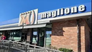 Ingresso del ristorante self-service Maglione a Moncalieri, con insegna visibile sulla facciata in mattoni rossi e clienti all’esterno, prima della chiusura definitiva avvenuta nel 2025.
