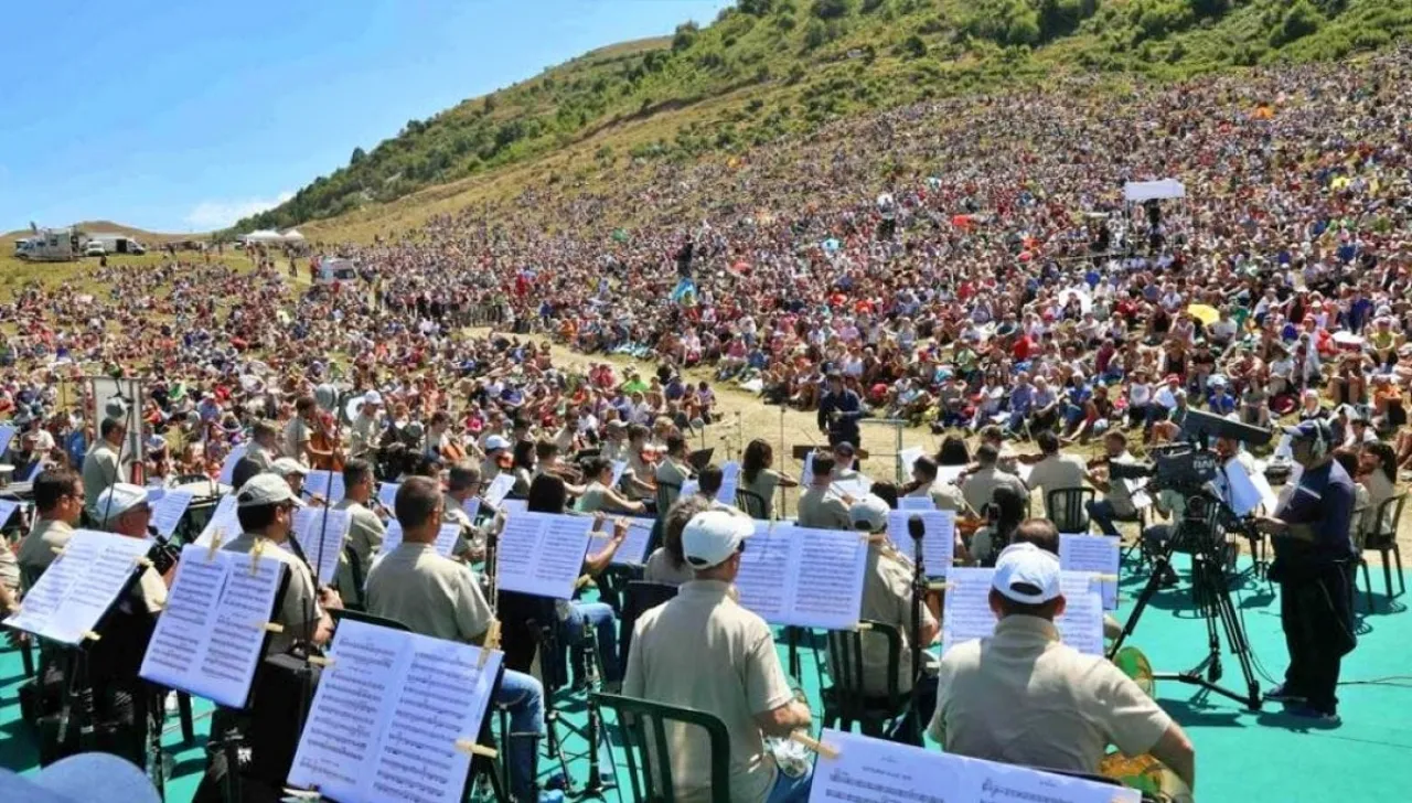 Concerto sinfonico all’aperto con orchestra sul palco panoramico e pubblico seduto sul prato, durante un evento
