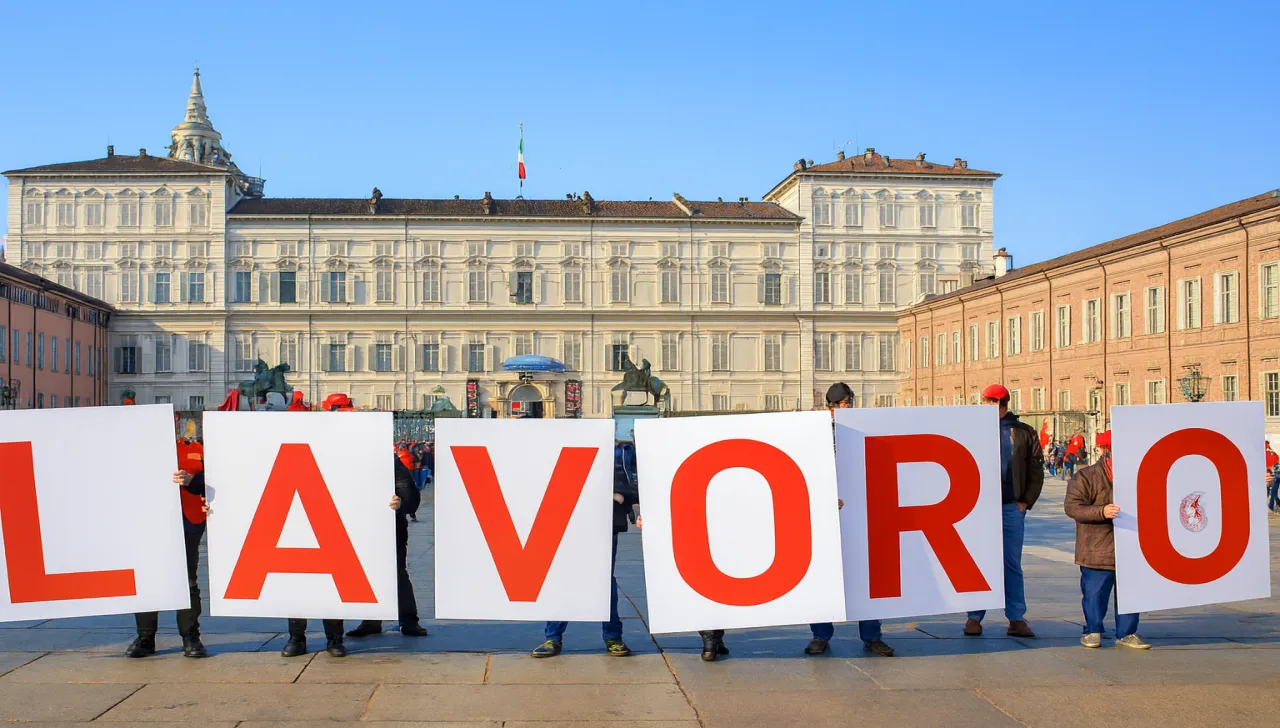 Manifestazione in piazza Castello a Torino con persone che reggono cartelli formando la scritta LAVORO, in riferimento ai dati sulla cassa integrazione in Piemonte nel primo semestre 2025.