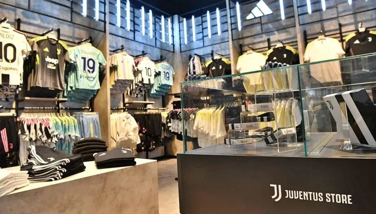 Interno del nuovo Juventus Store al Centro Commerciale Le Gru di Grugliasco, con esposizione di maglie ufficiali, abbigliamento e gadget bianconeri.