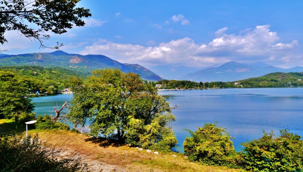 Panorama del Lago Grande di Avigliana circondato da alberi e montagne sotto un cielo azzurro
