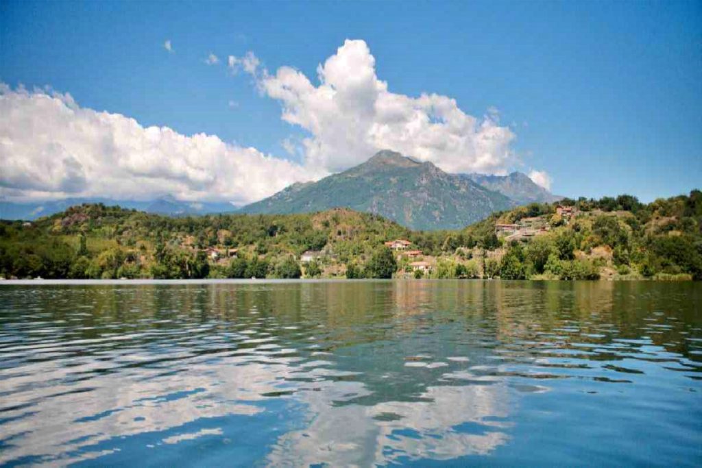 Vista del Lago Sirio con acque tranquille, colline verdi circostanti e montagne sullo sfondo sotto un cielo azzurro con nuvole bianche