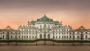 Facciata principale della Palazzina di Caccia di Stupinigi al tramonto, con il cancello in ferro battuto in primo piano e il cielo rosaceoo sullo sfondo.