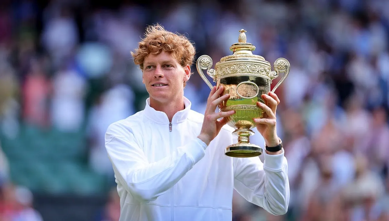 Jannik sinner su un campo da tennis, vestito di bianco, che mostra orgoglioso la coppa per aver vinto Wimbledon