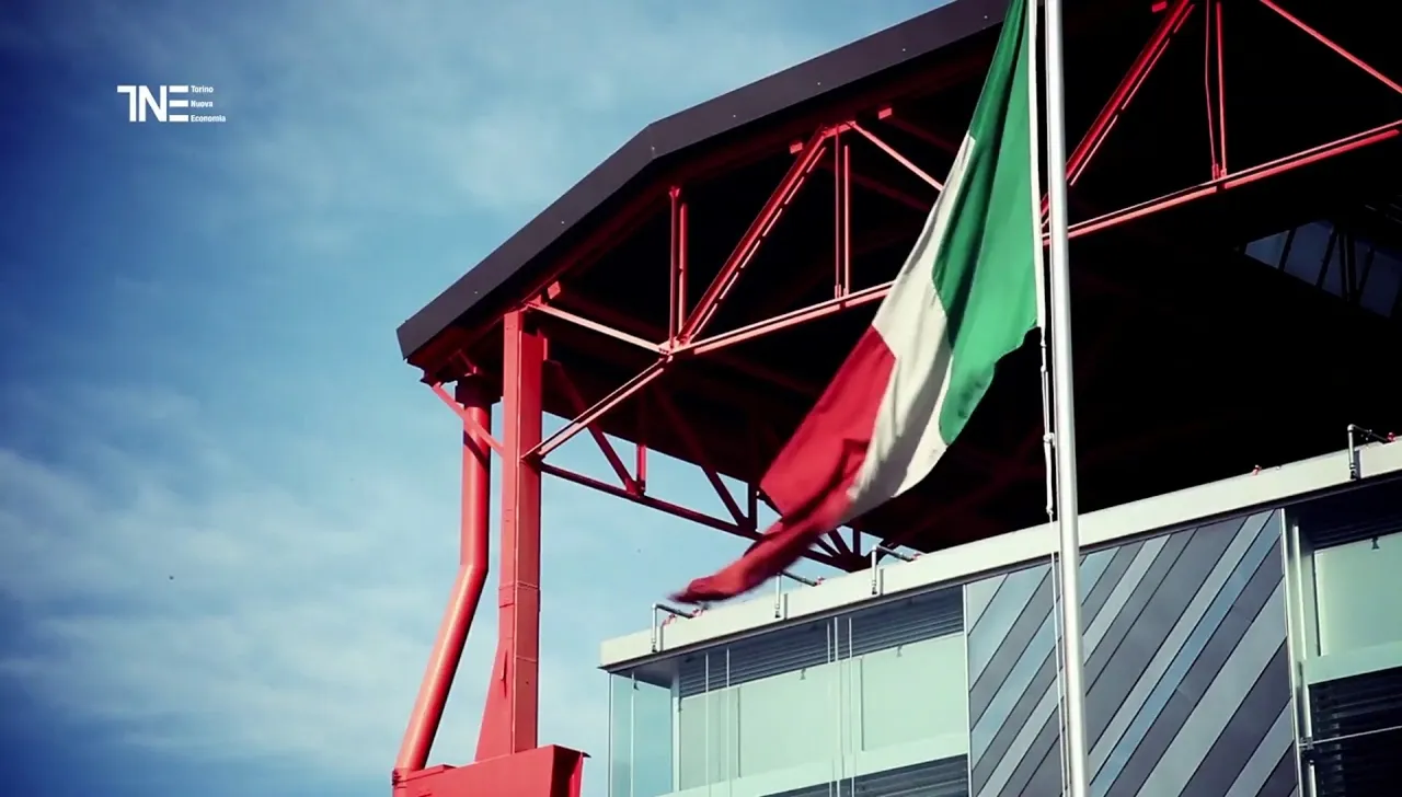 Vista dell’edificio ristrutturato di Torino Nuova Economia con struttura rossa industriale e bandiera italiana in primo piano